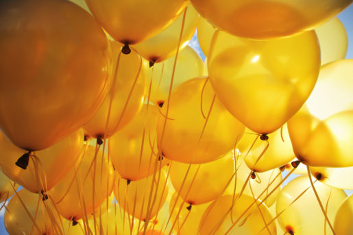 Background of bright yellow inflatable balloons up in the air, backlit by sun.