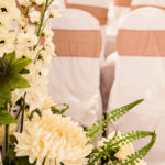 White wedding bouquet in the foreground with chairs in background arranged in rows and dressed with ribbons