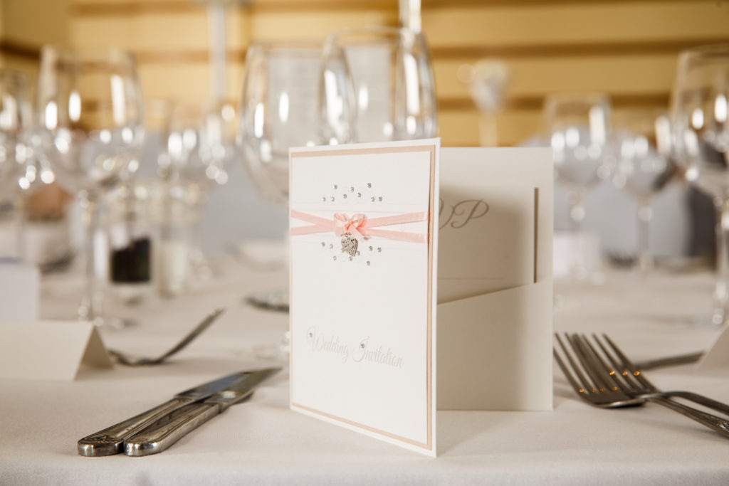 Close up of a wedding invitation in front of a place setting for a wedding at mercure hotels
